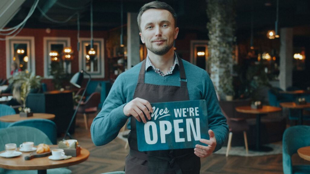 Cafe owner holding a We're Open sign inside a coffee shop